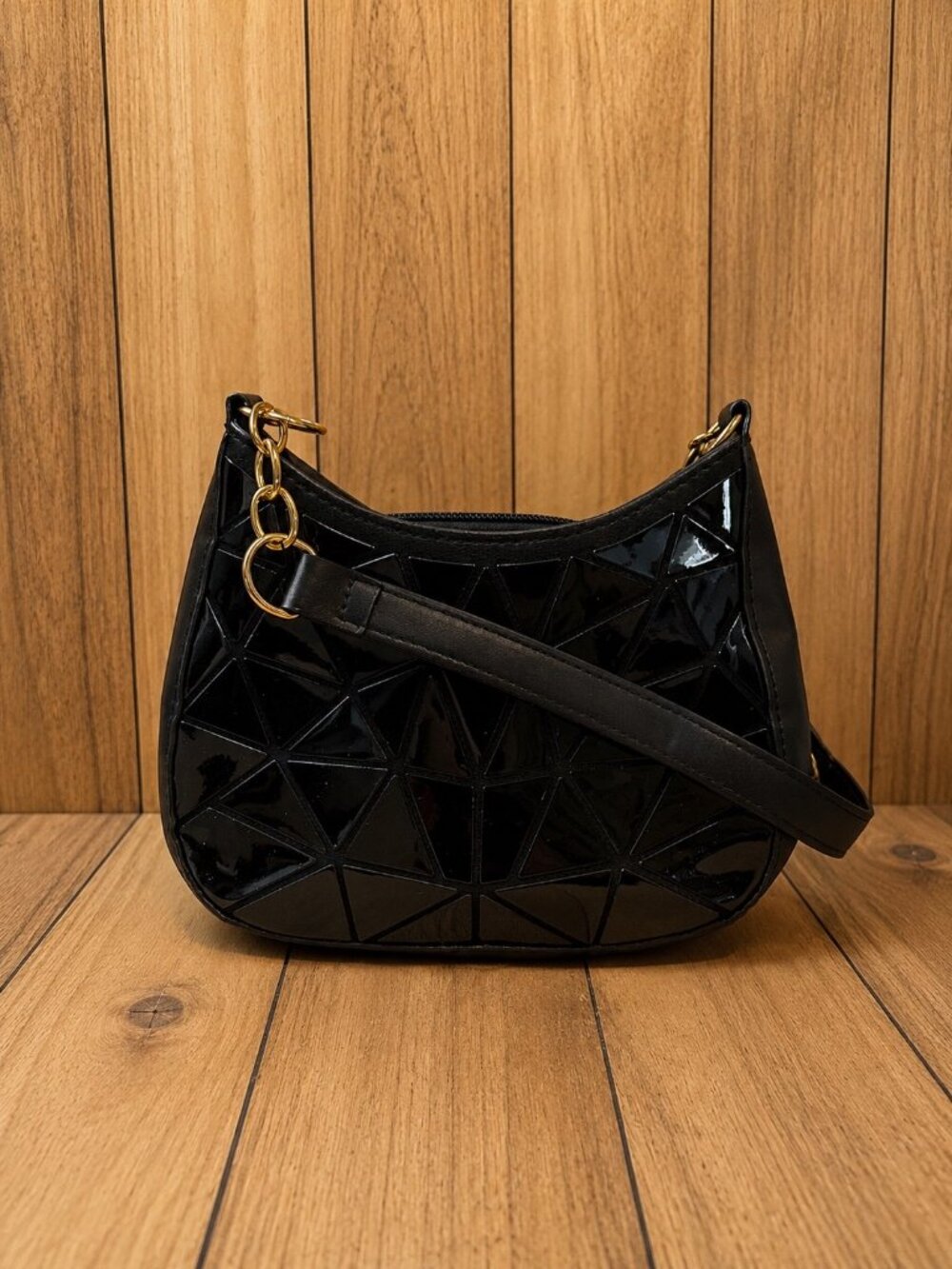 Black crescent-shaped shoulder bag featuring a glossy geometric front design
